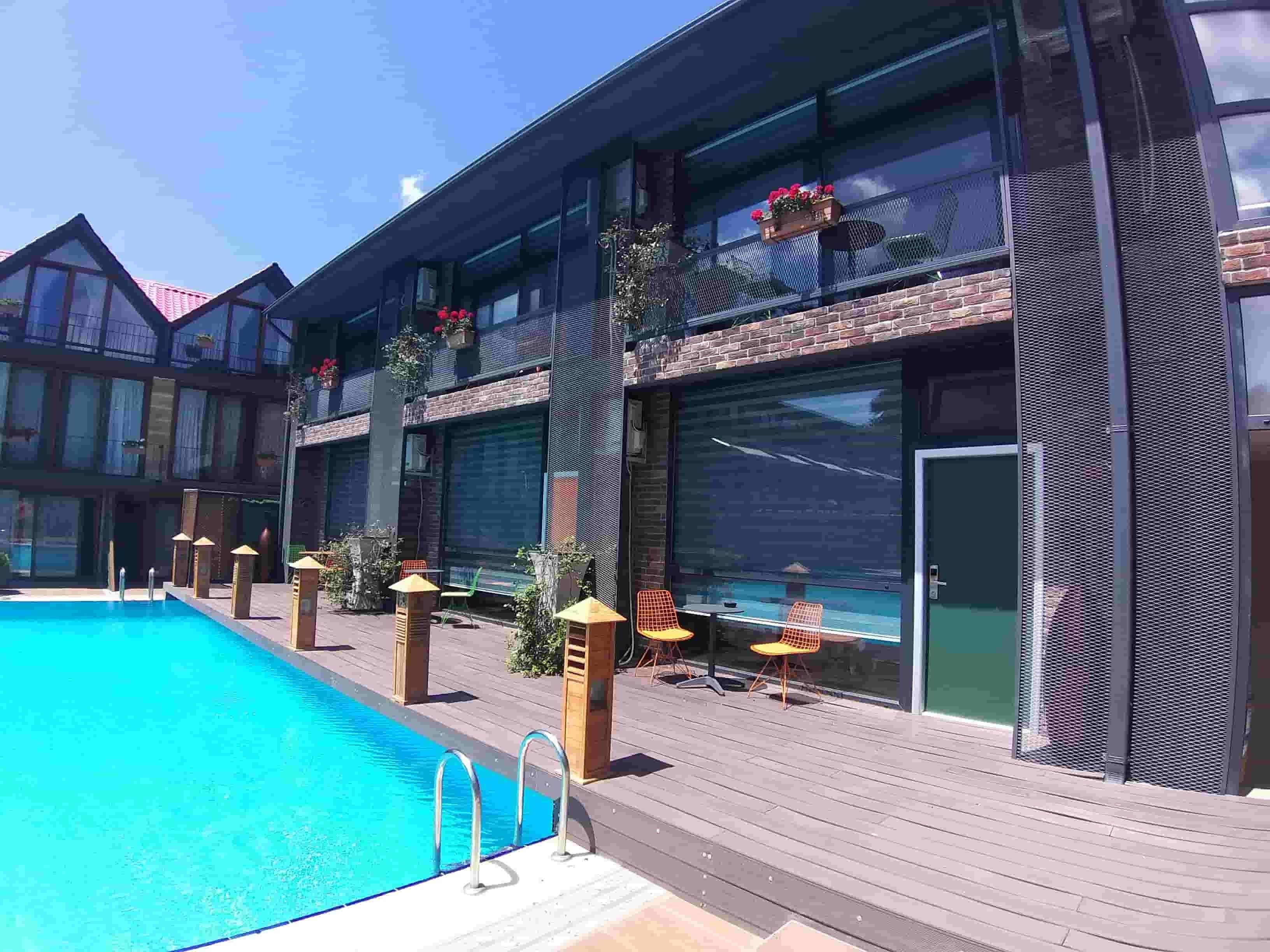 A modern hotel with a swimming pool, outdoor seating, and large windows.
