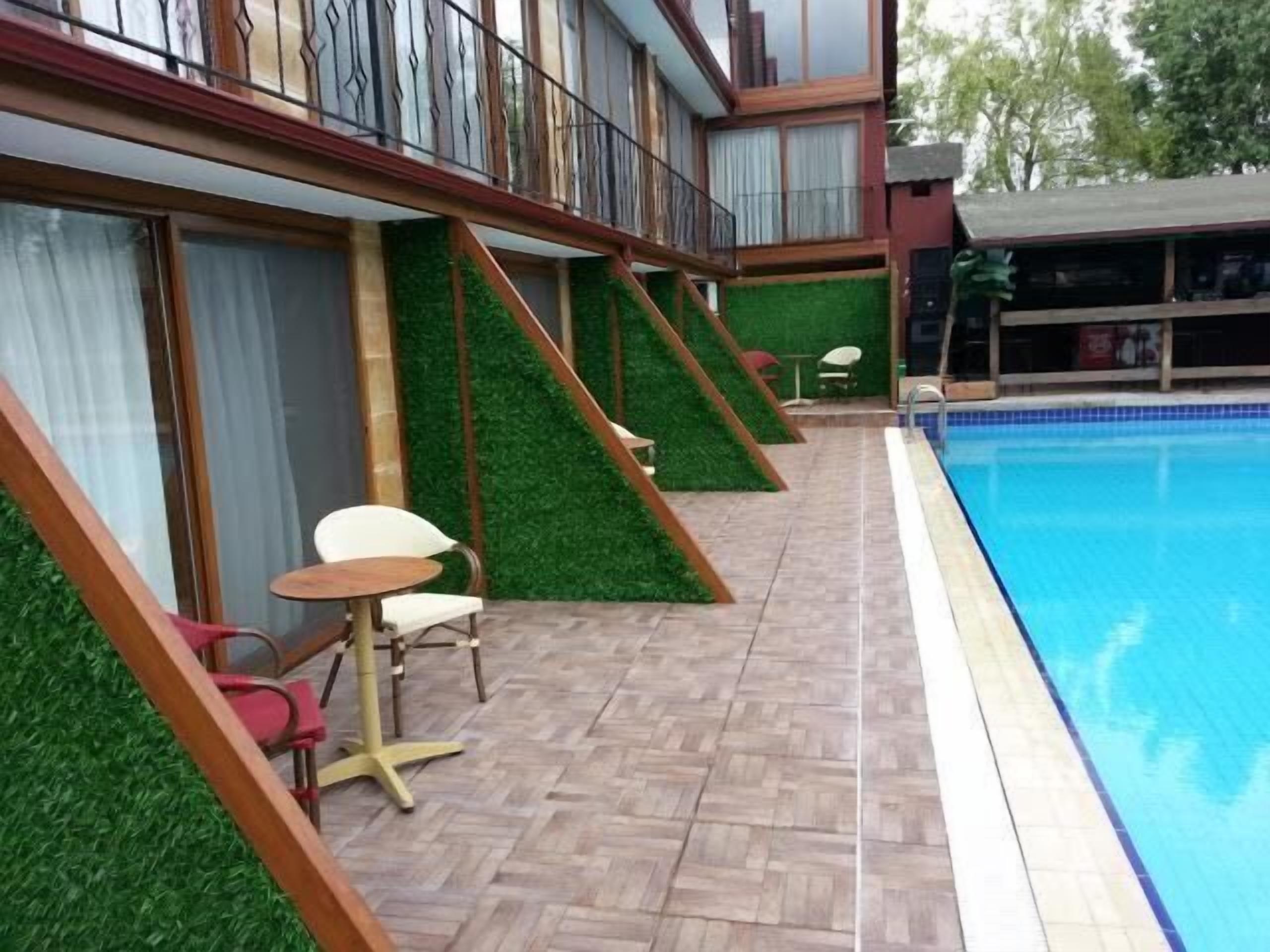 A poolside area with a wooden deck, a pool, and a small seating area with chairs and a table.