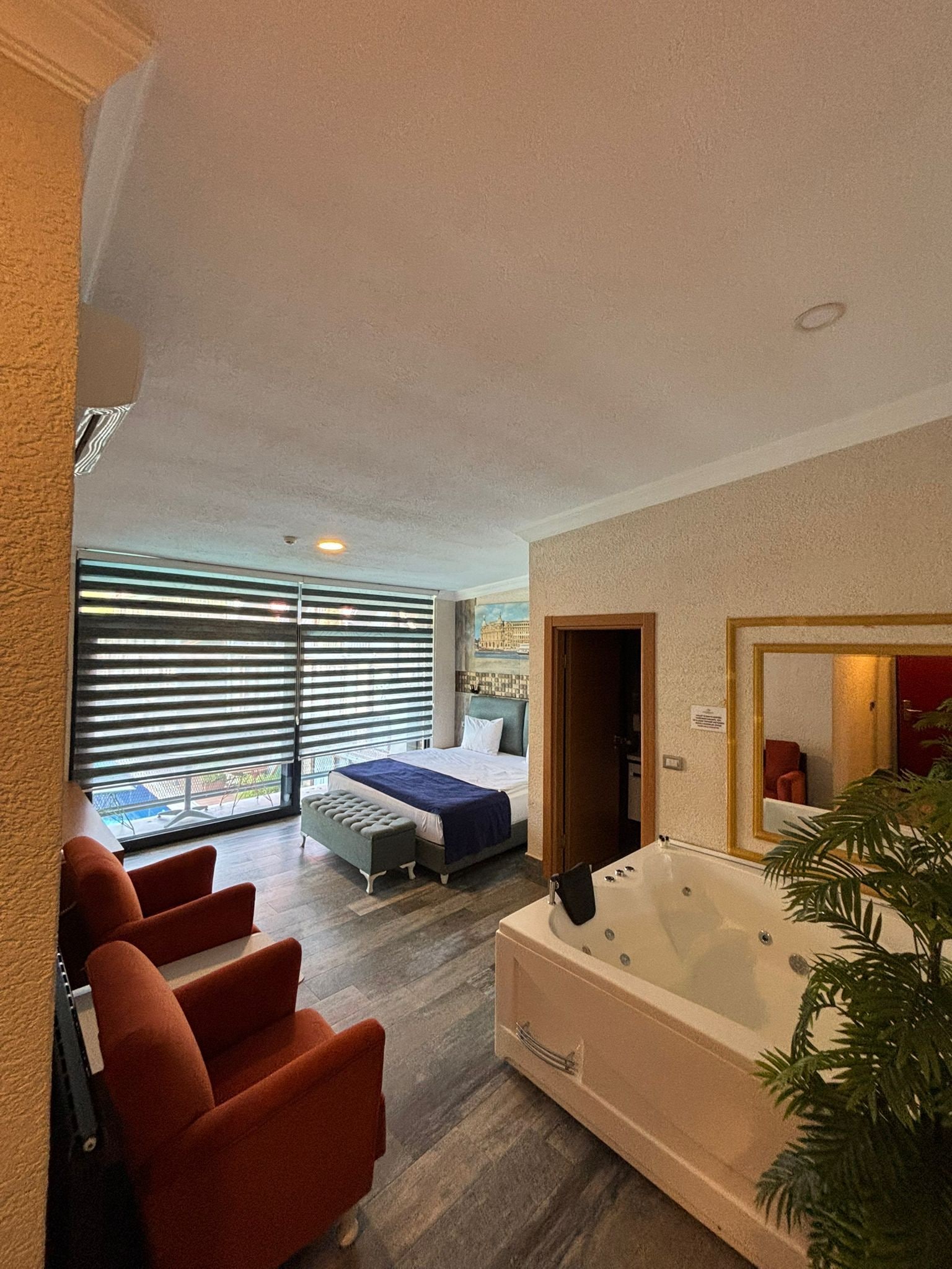 Una habitación de hotel moderna con una cama grande, un rincón de estar con sillas, una bañera y vistas por la ventana.