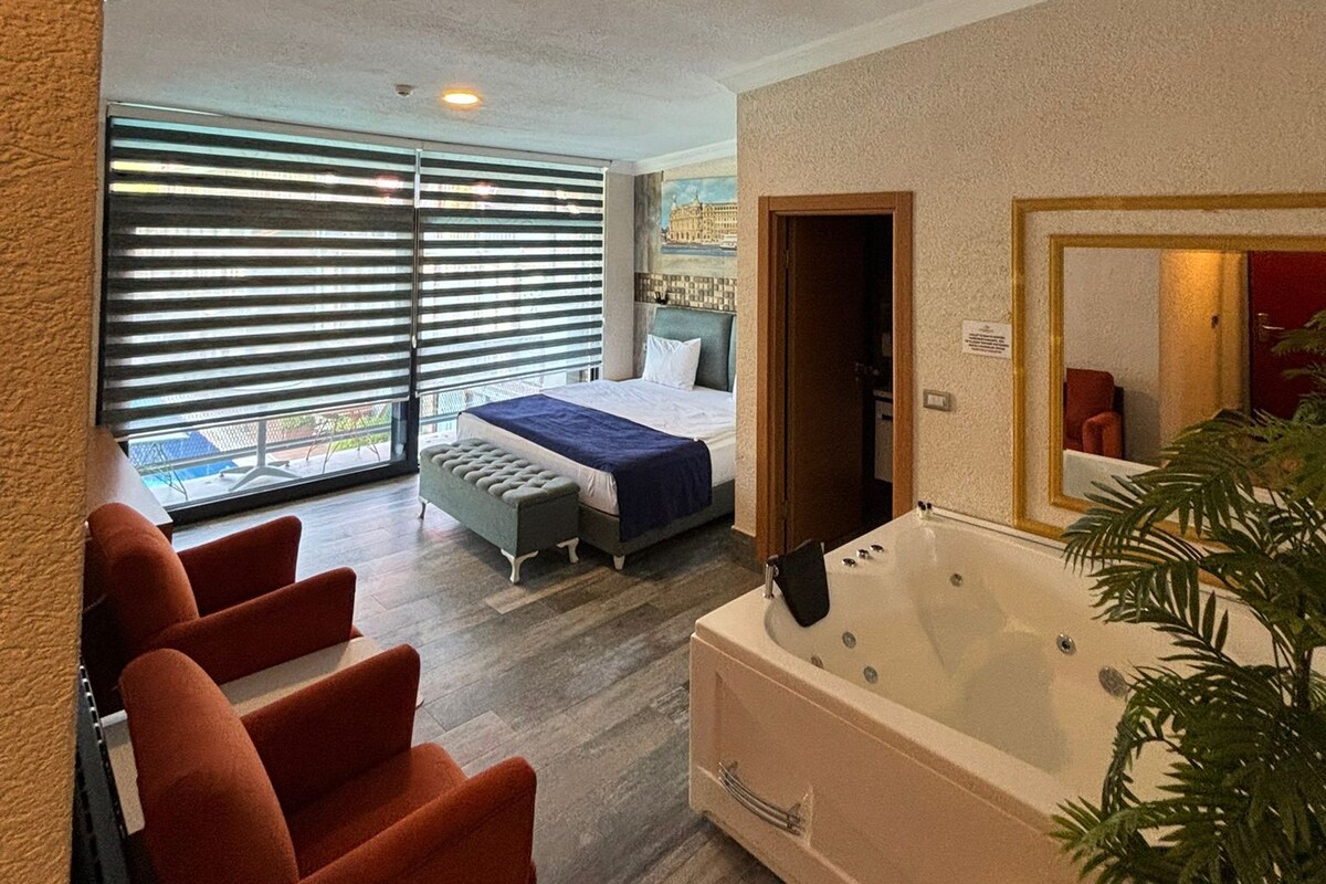 Una habitación de hotel moderna con una cama grande, un rincón de estar con sillas, una bañera y vistas por la ventana.