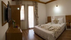 A hotel room with a large bed, a wooden dresser, a TV, and a window with curtains. - Portofino Hotel (Ula)