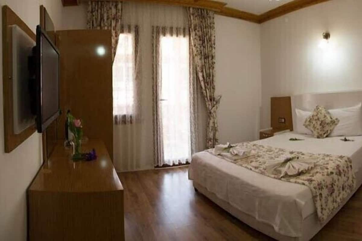 Camera d'albergo con un letto grande, un settimino in legno, una TV e una finestra con tende.