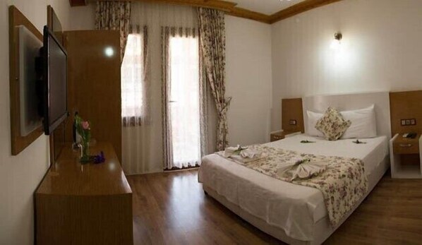 Une chambre d’hôtel avec un grand lit, une commode en bois, une télévision et une fenêtre avec des rideaux.