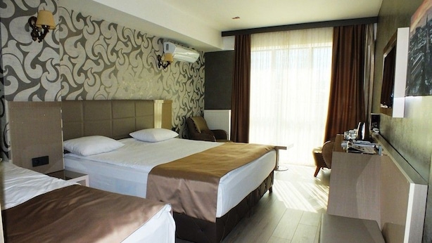 A hotel room with two beds, a desk, a chair, a TV, and a window with curtains. - Colonia Park Hotel (Sebinkarahisar)