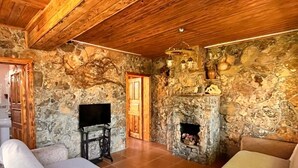 A rustic interior with stone walls, wooden ceiling beams, a fireplace, and two sofas.