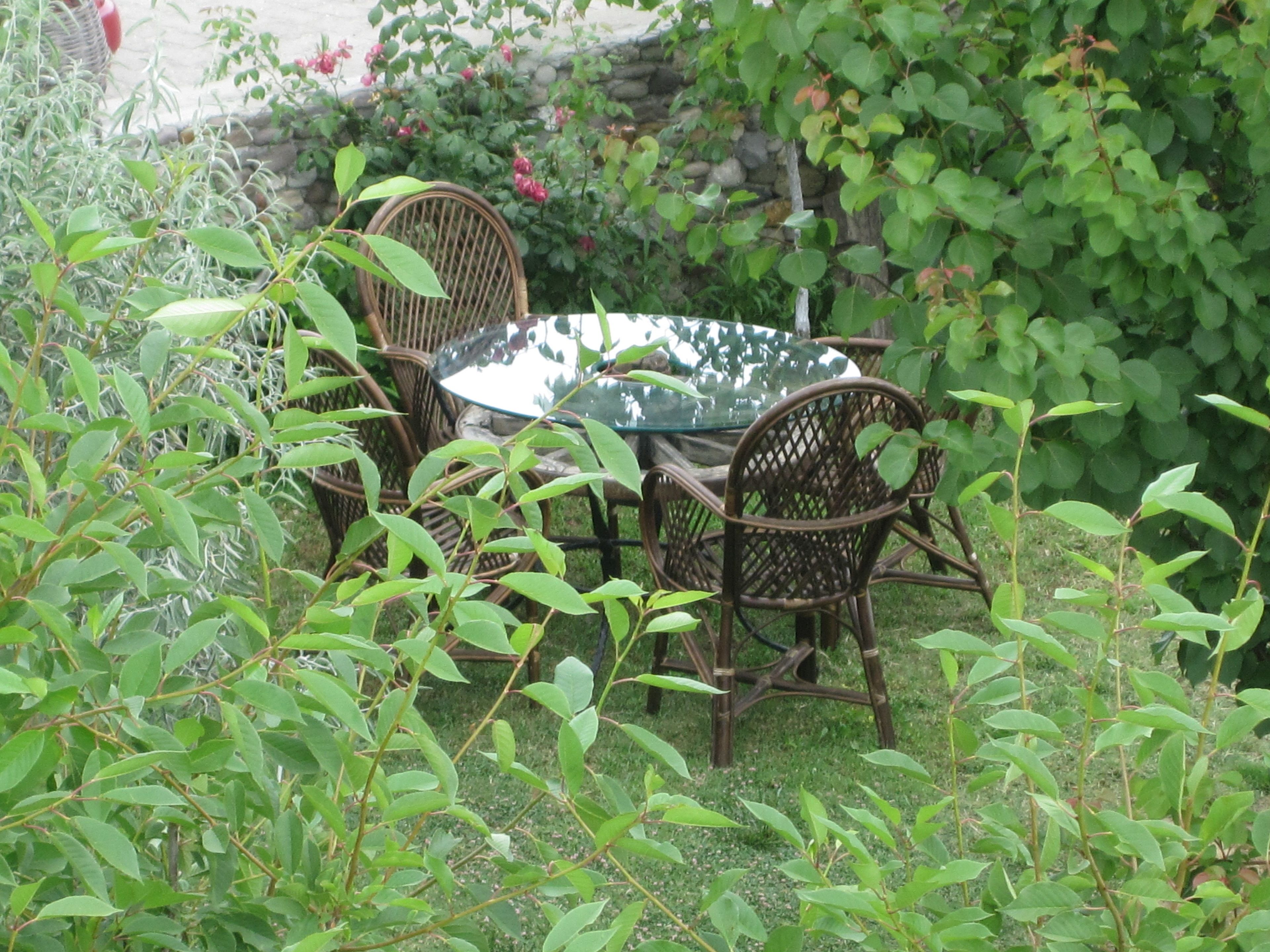 A round glass table with wicker chairs in a garden setting.