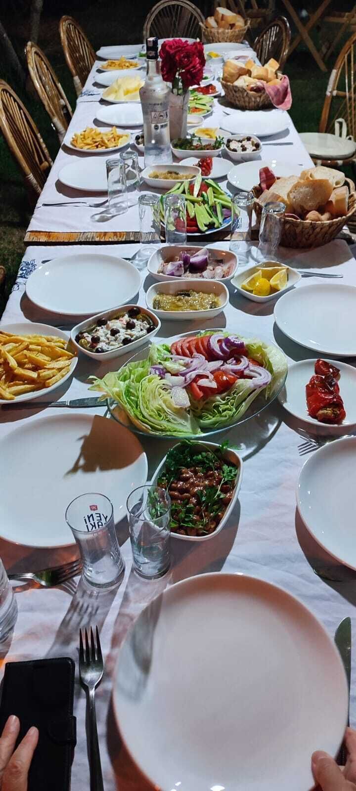 Una mesa de comedor dispuesta con varios platos, entre ellos ensaladas, pan y una botella de agua.