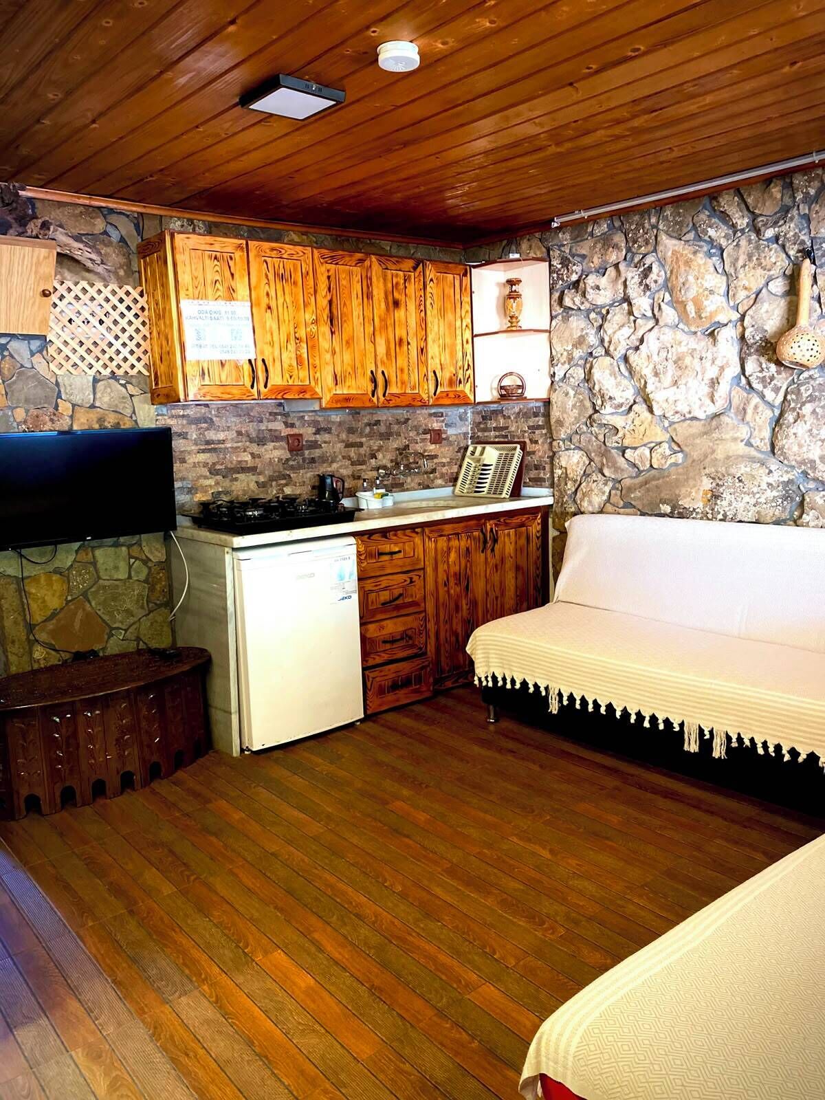 Eine kleine Küche mit Holzausstattung, einer Steinwand, einem weißen Kühlschrank und einer Couch.