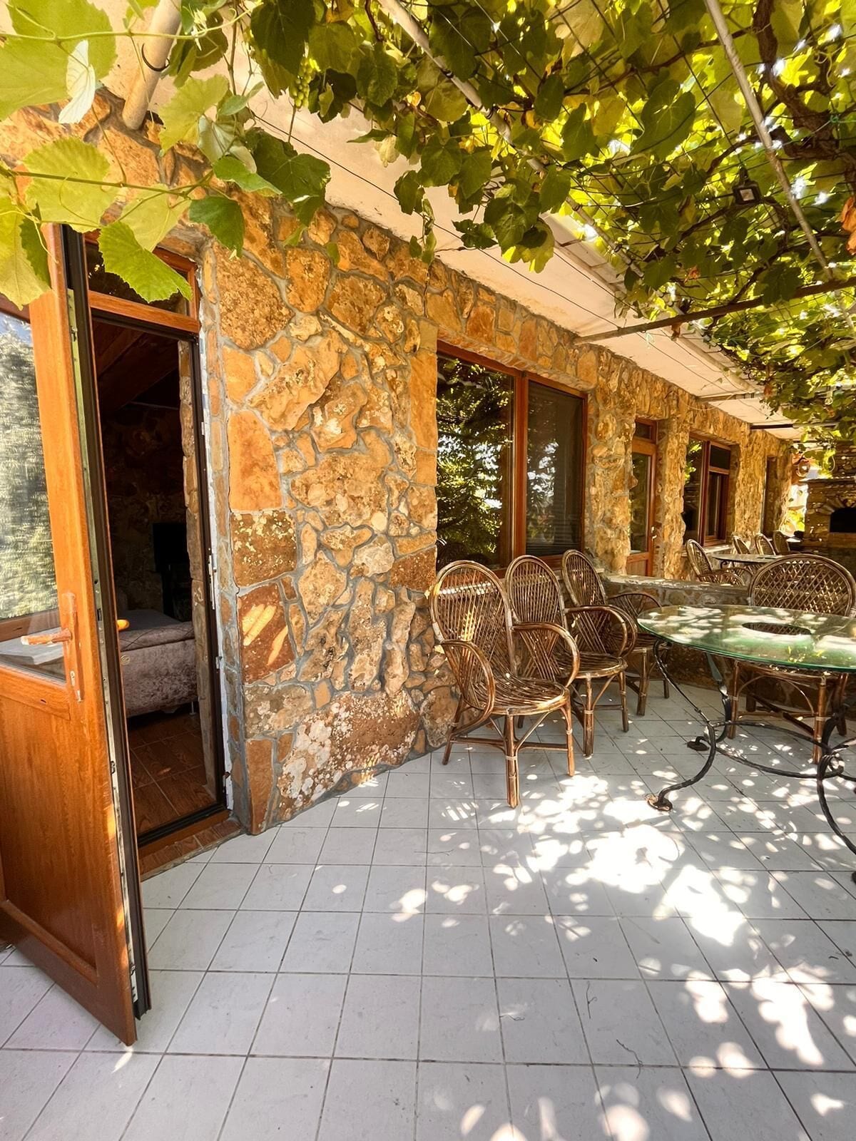 A stone-walled patio with wicker furniture and a glass table, surrounded by a covered area with natural light.