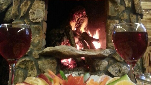 A stone fireplace with a fire, two wine glasses, and a fruit platter.