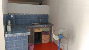 A small kitchen with blue tiles, a sink, a fan, and a few drawers.