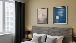Een moderne hotelkamer met een groot bed, twee nachtkastjes, een raam met gordijnen en twee ingelijste foto's aan de muur.