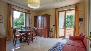 A spacious living room with a red sofa, a wooden dining table with chairs, a cabinet, and a large window with curtains. - Relais Villa Jacopone Suites (Florence)