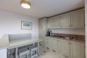 Una cocina con armarios blancos, una mesa de vidrio y una cafetera.