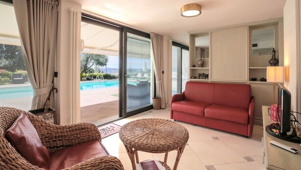 A room with a red sofa, wicker chairs, a small table, and a TV. There is a sliding glass door leading to a pool area. - Relais Villa Jacopone Suites (Florence)