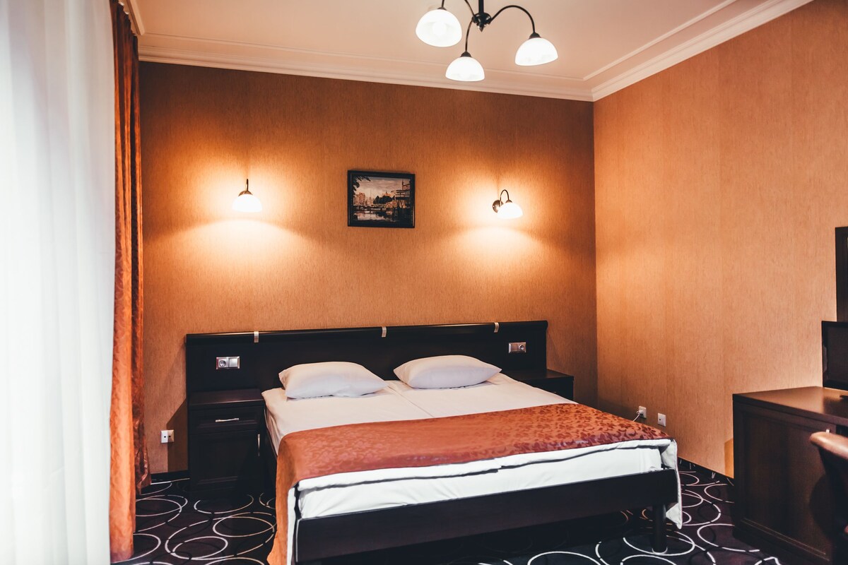 Una habitación de hotel con cama, mesitas de noche, lámpara y un cuadro en la pared.