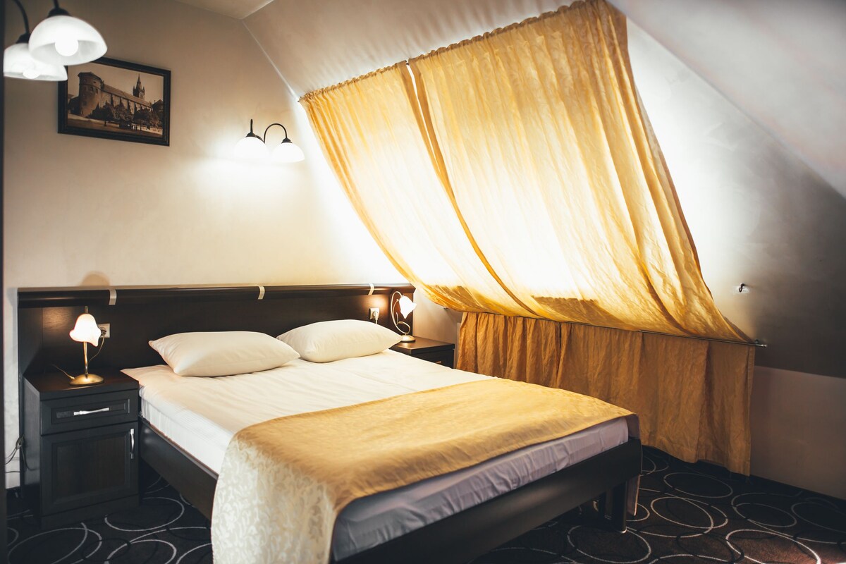 Una habitación de hotel con cama, mesitas de noche, lámpara y cortina.