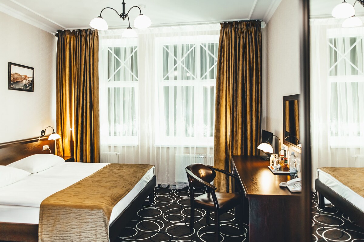 Habitación de hotel con dos camas, un escritorio con silla, un espejo y una ventana con cortinas.