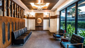 A modern lobby with a wooden reception desk, a seating area with sofas, a decorative wall, and a large window offering a view of the outdoors. - B2 Nimman Premier Hotel (Chiang Mai)