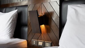 A modern hotel room with a geometric-patterned headboard, a bedside table, and a nightstand with a lamp. There are three electrical outlets on the wall. - B2 Nimman Premier Hotel (Chiang Mai)