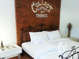 Un dormitorio con pared de ladrillo, una cama con ropa de cama blanca, una mesita de noche con lámpara y un cartel decorativo que dice 