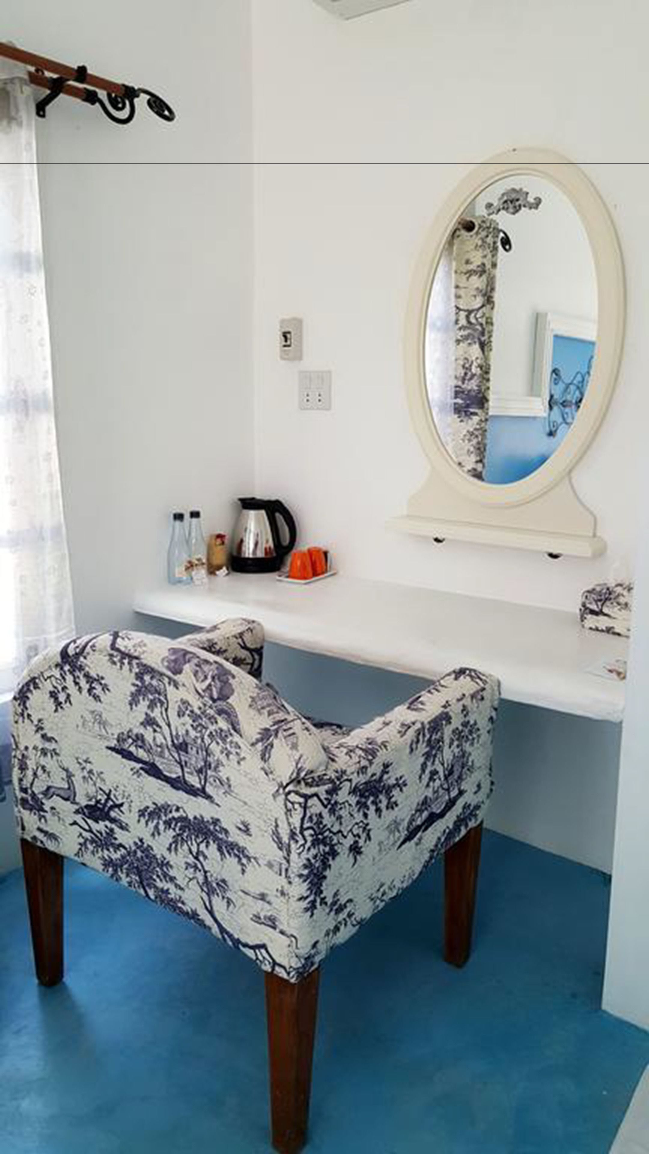 Una habitación con un escritorio blanco, una silla con estampado floral, un espejo, una tetera y una cafetera.