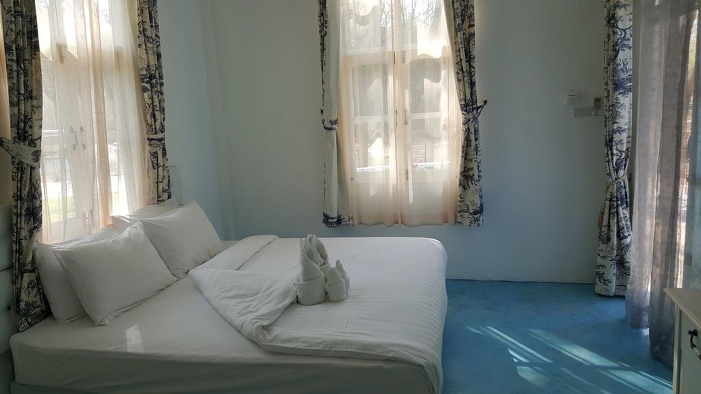 A bedroom with a bed, white curtains, and a blue floor.