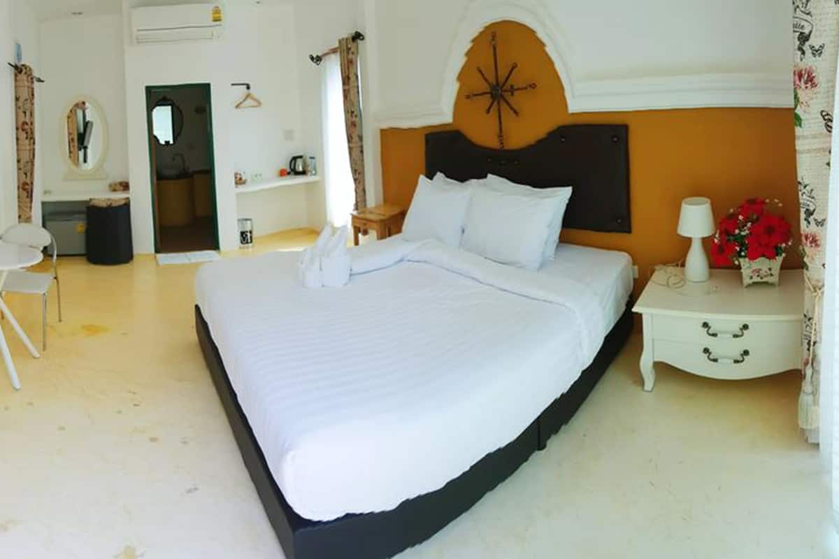 A bedroom with a large bed, a bedside table with a lamp, a chair, and a small table with a vase of flowers.