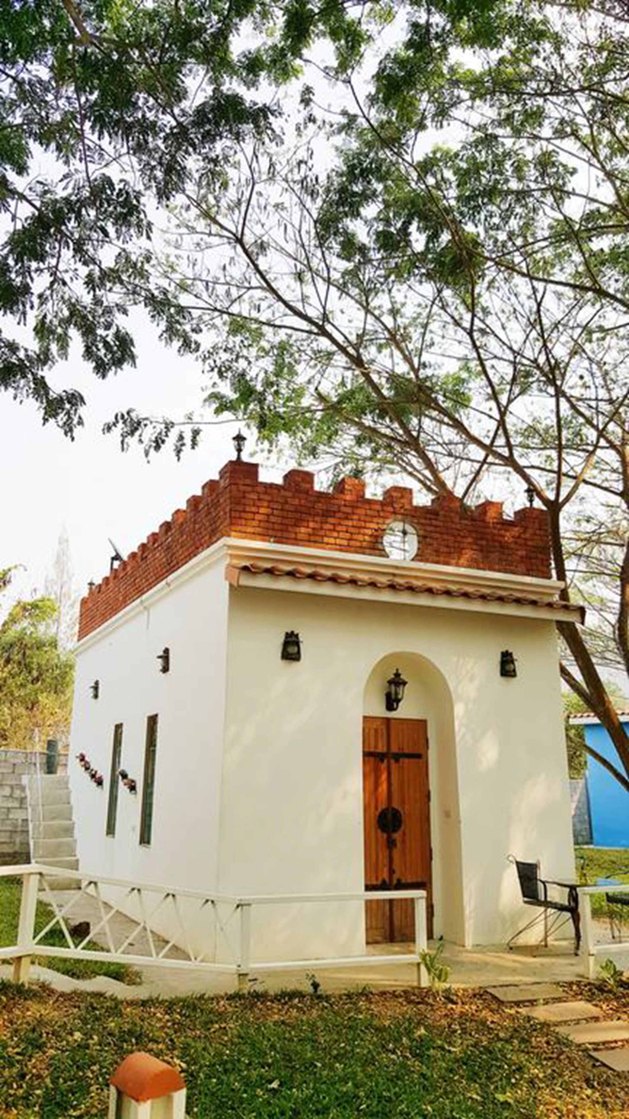 A small, single-story building with a white exterior and a red-tiled roof. It features a wooden door and a small porch area.