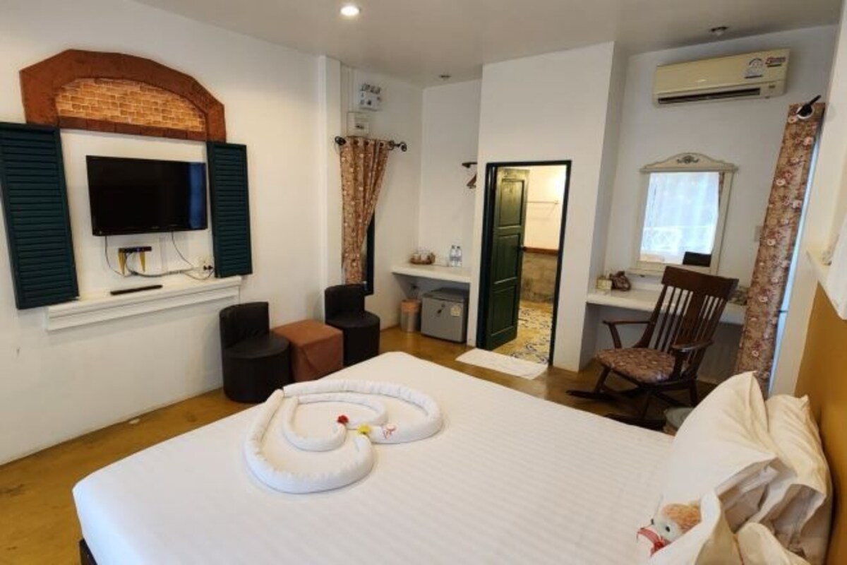 A hotel room with a bed, a television, a desk, a chair, and an air conditioning unit.