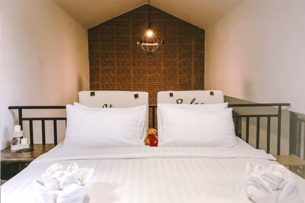 A double bed with white linens, a brick wall, and a hanging light fixture.