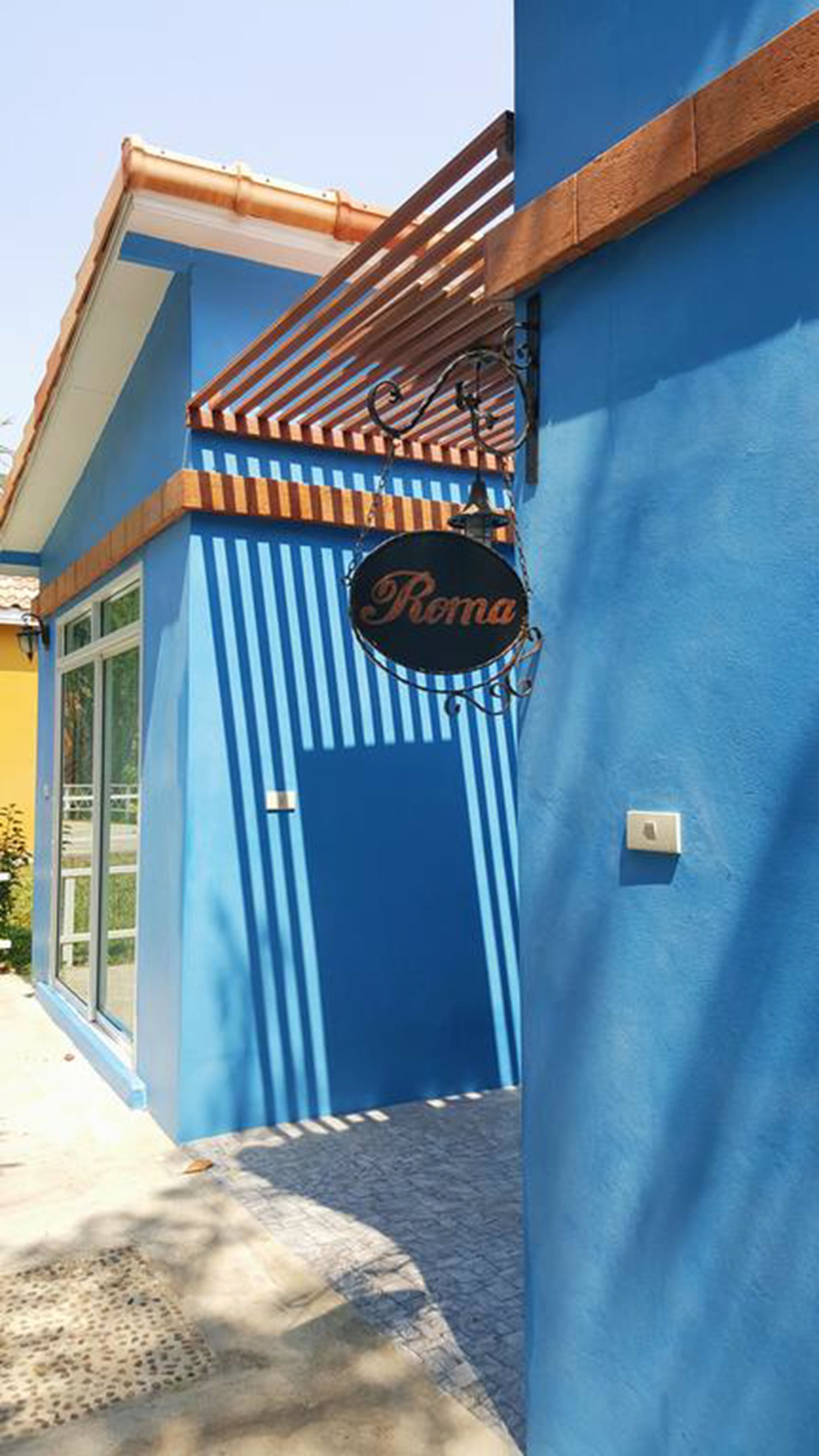 Un edificio con fachada azul, un toldo de listones de madera y un letrero que dice "Roma".