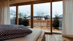 A bedroom with a large window, wooden flooring, and a bed with checkered bedding. - Flora - Das kleine Gartenhotel (Ellmau)