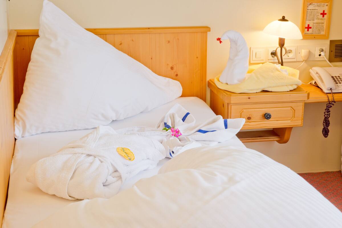 A neatly made bed with white linens, a pillow, a bedside table with a lamp, and a phone.