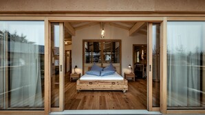 A spacious bedroom with a large bed, wooden flooring, and sliding glass doors leading to a balcony. - Flora - Das kleine Gartenhotel (Ellmau)