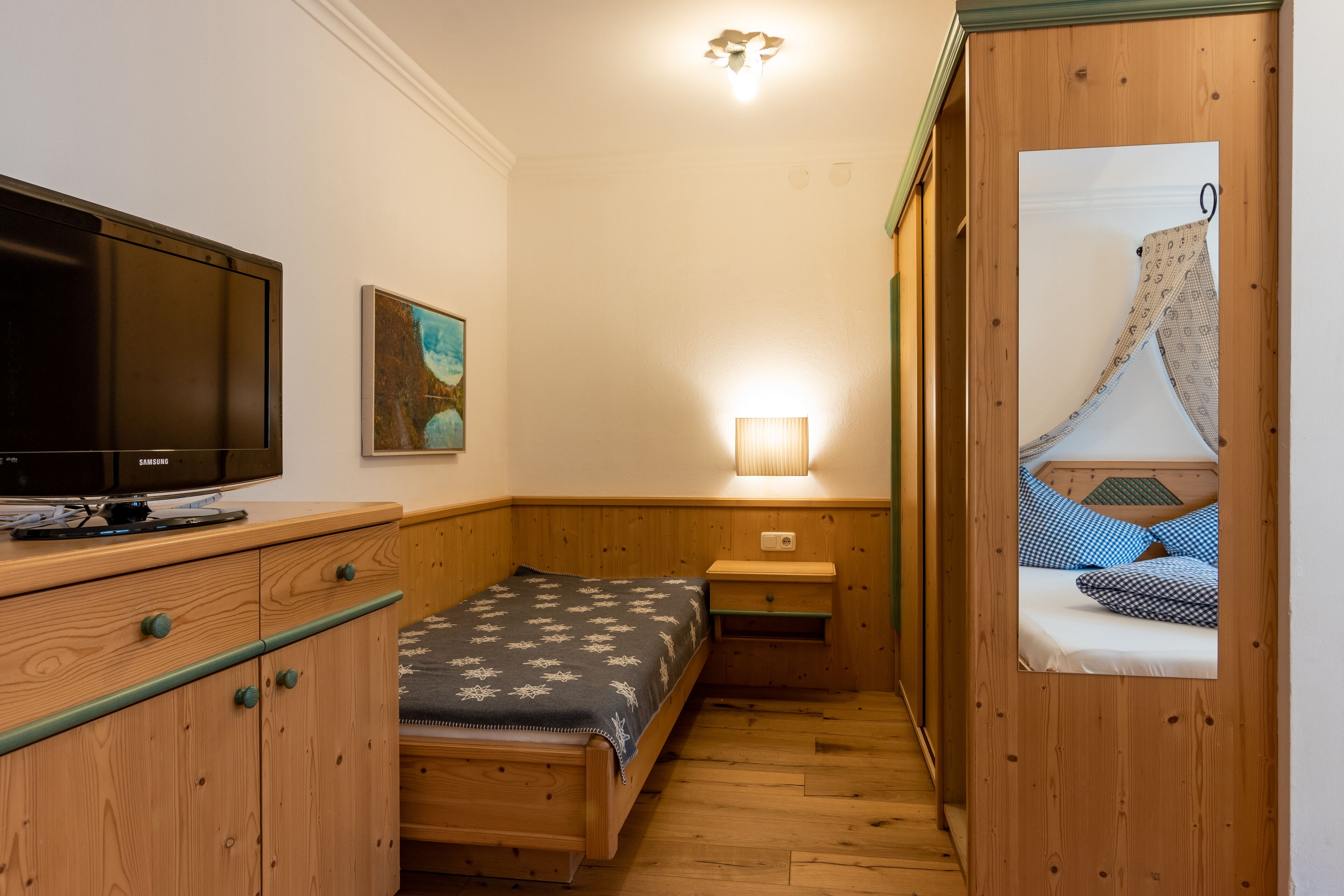 Una habitación pequeña y acogedora con una cama, un televisor, una mesita de noche y una lámpara.