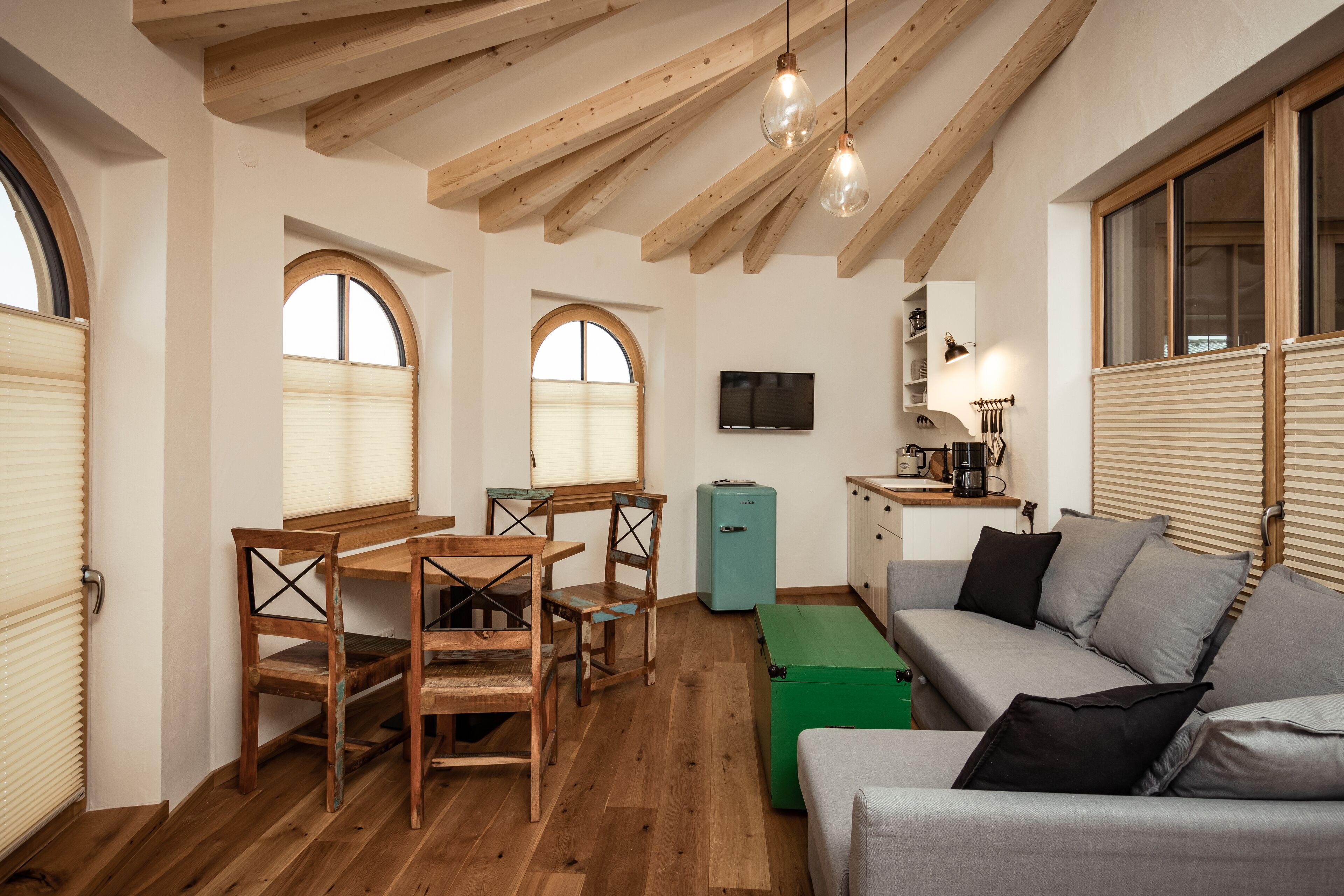 Une pièce chaleureuse avec des poutres apparentes, une table à manger avec des chaises, un canapé et un téléviseur.