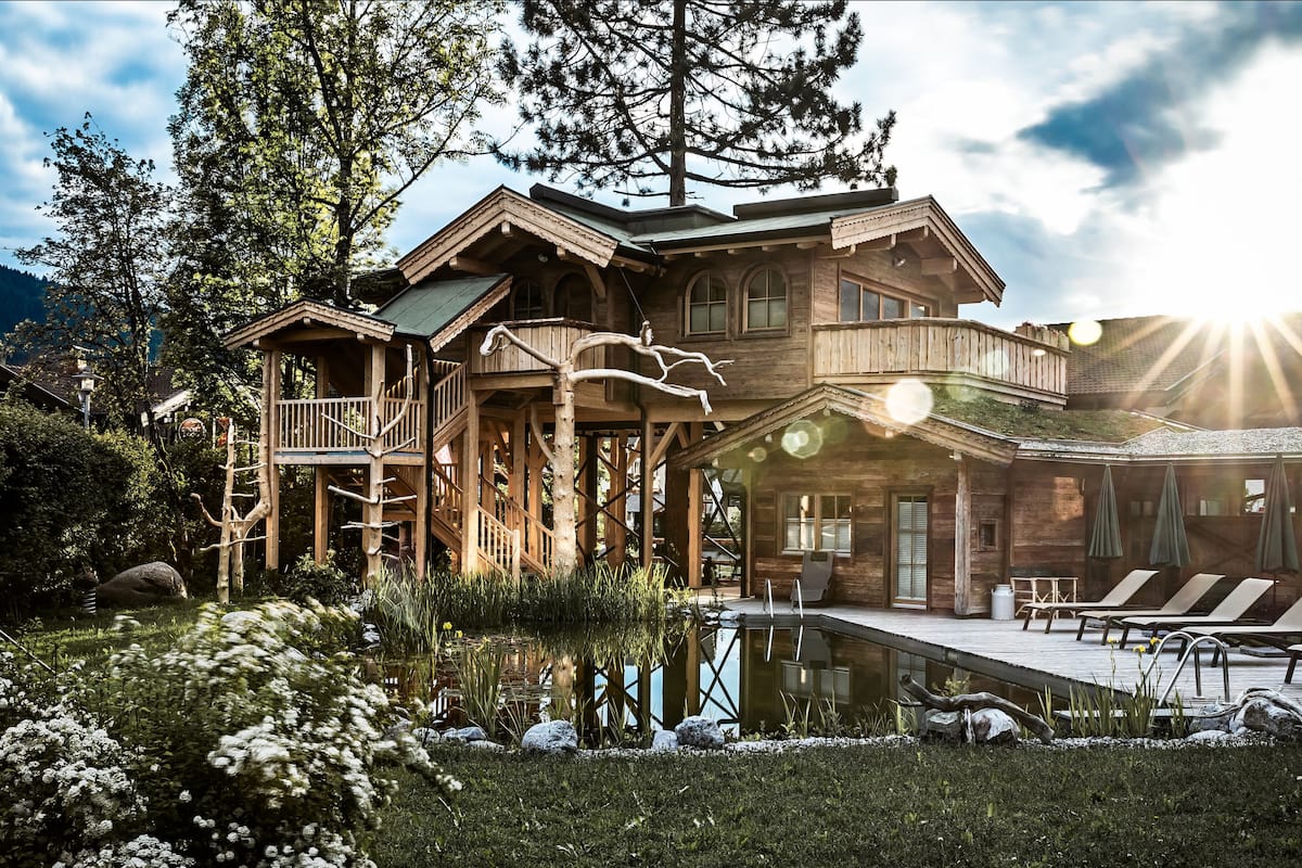 A large wooden lodge with a swimming pool, outdoor seating, and a scenic mountain backdrop.