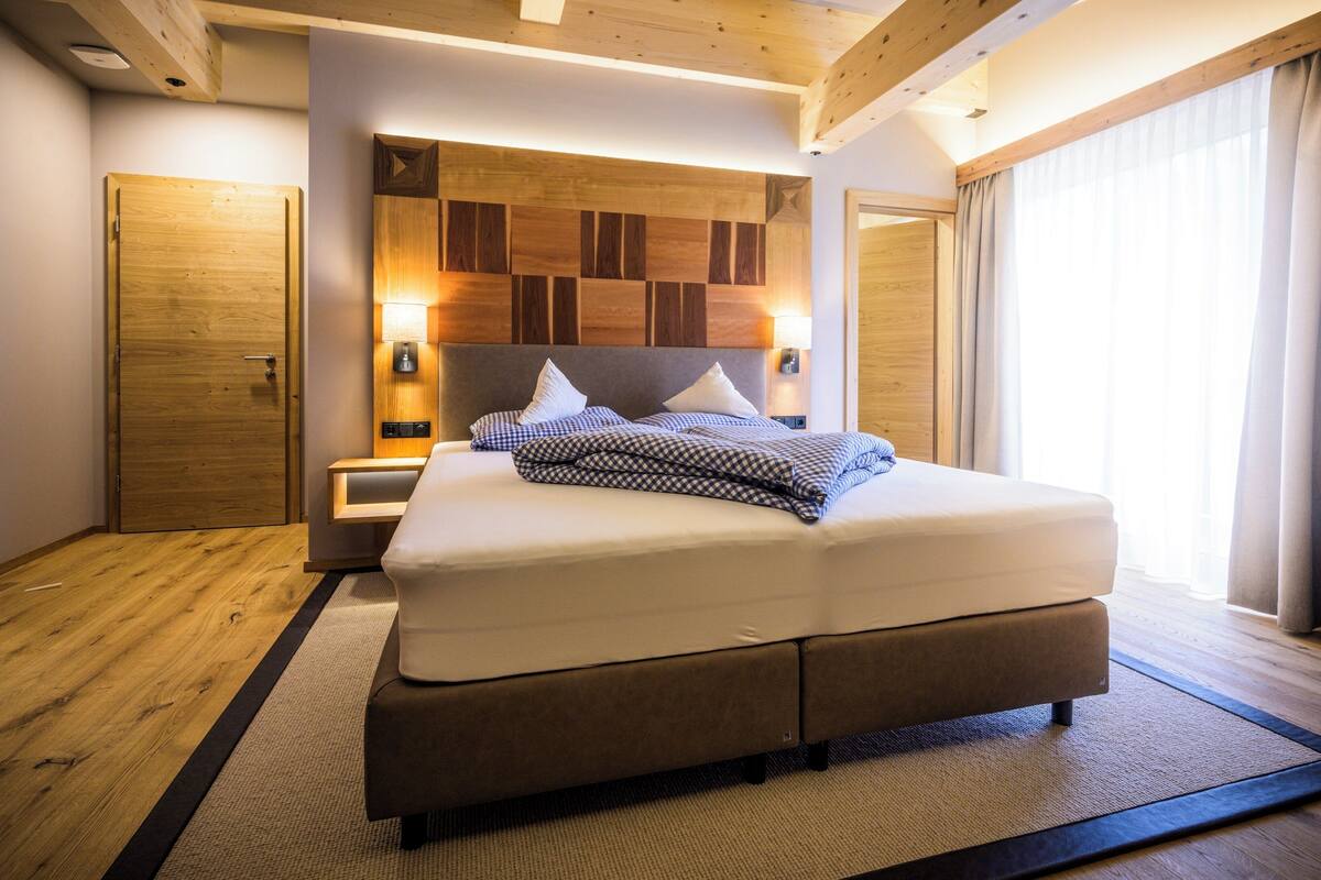 A modern bedroom with a large bed, wooden headboard, bedside lamps, and a view of the outdoors.