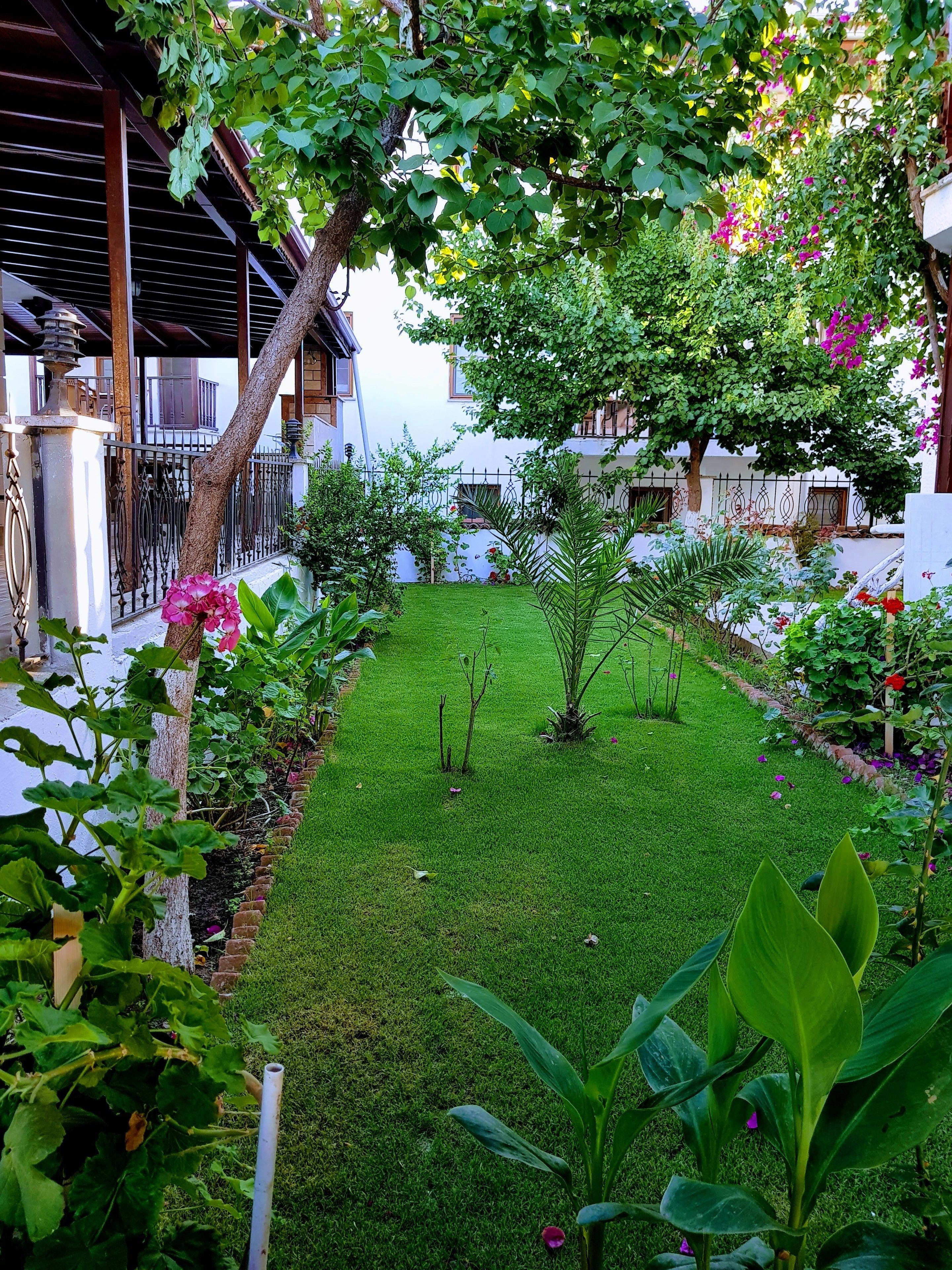 A well-maintained garden with a variety of plants and flowers, a neatly trimmed lawn, and a building with a balcony in the background.