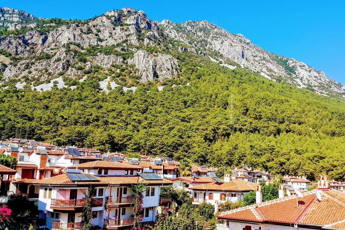 A coastal village with traditional Mediterranean architecture, terraced houses, and a mountainous backdrop.
