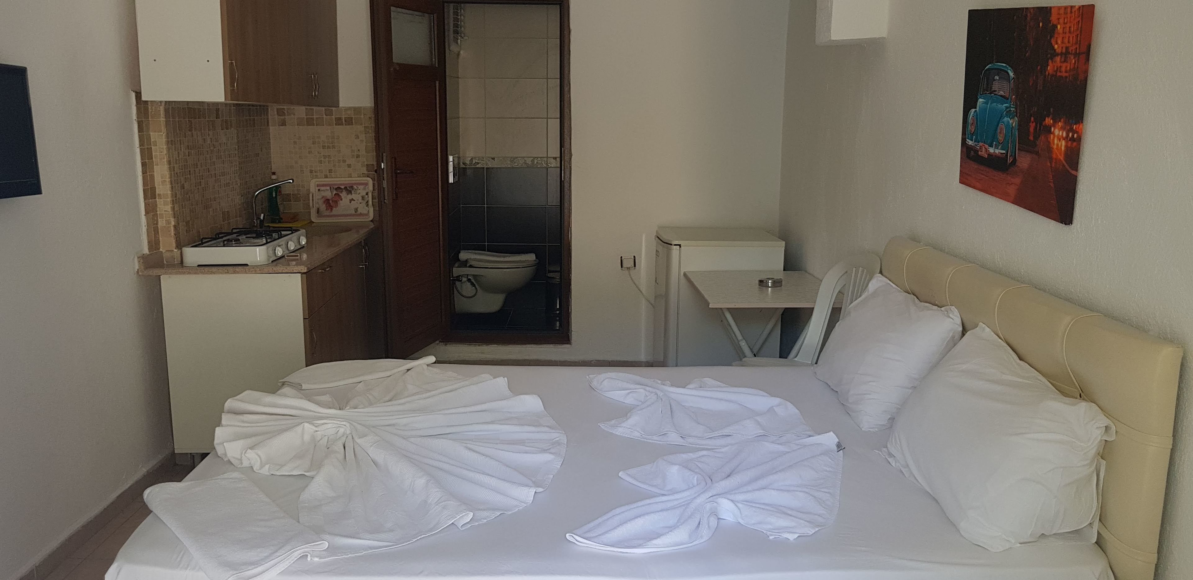 Habitación de hotel con cama, kitchenette pequeña, baño y un cuadro en la pared.