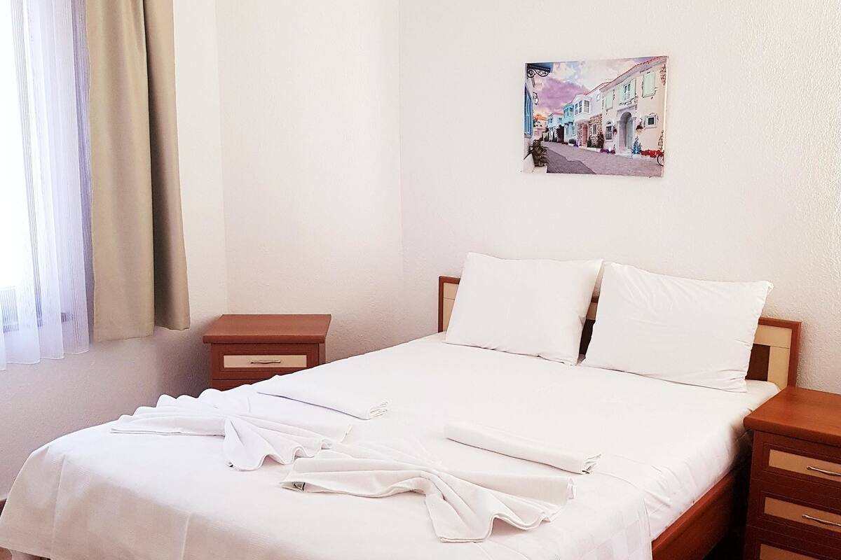 A neatly made bed with white linens, a wooden headboard, and two bedside tables with drawers.