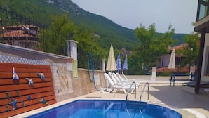 Piscina con deck de baldosas, sillas de descanso y vista a un paisaje montañoso.