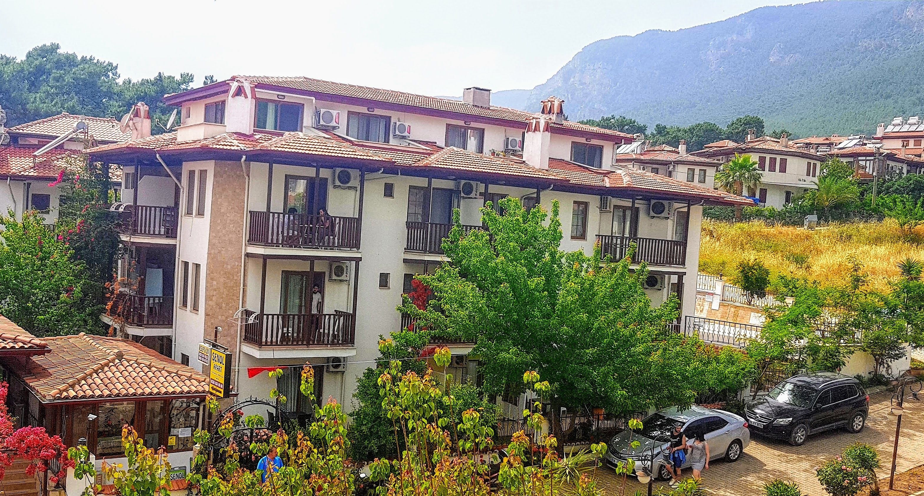 Un edificio residencial de varios pisos con balcones, rodeado de vegetación y un paisaje montañoso.