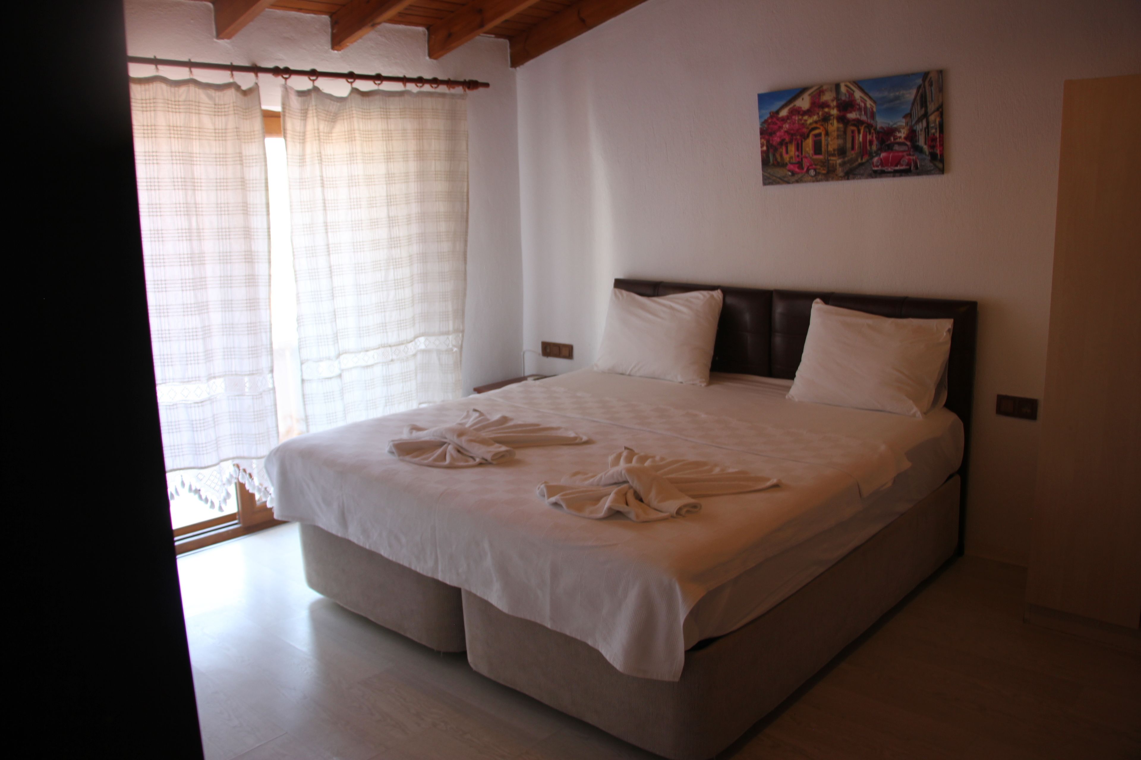 A bedroom with a large bed, white linens, and a painting on the wall.