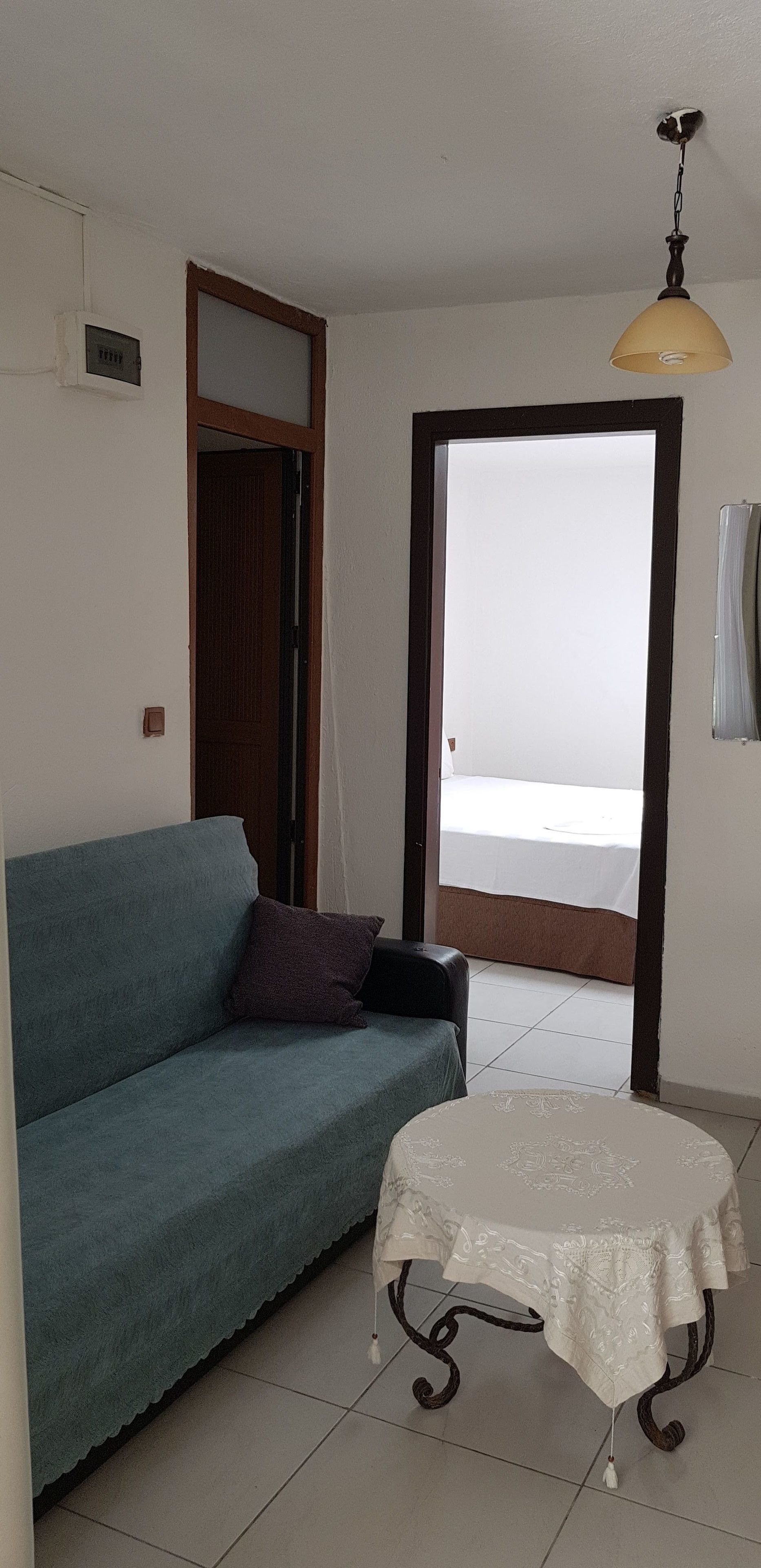 A room with a blue sofa, a small table with a white tablecloth, a ceiling light, and a door leading to a balcony.