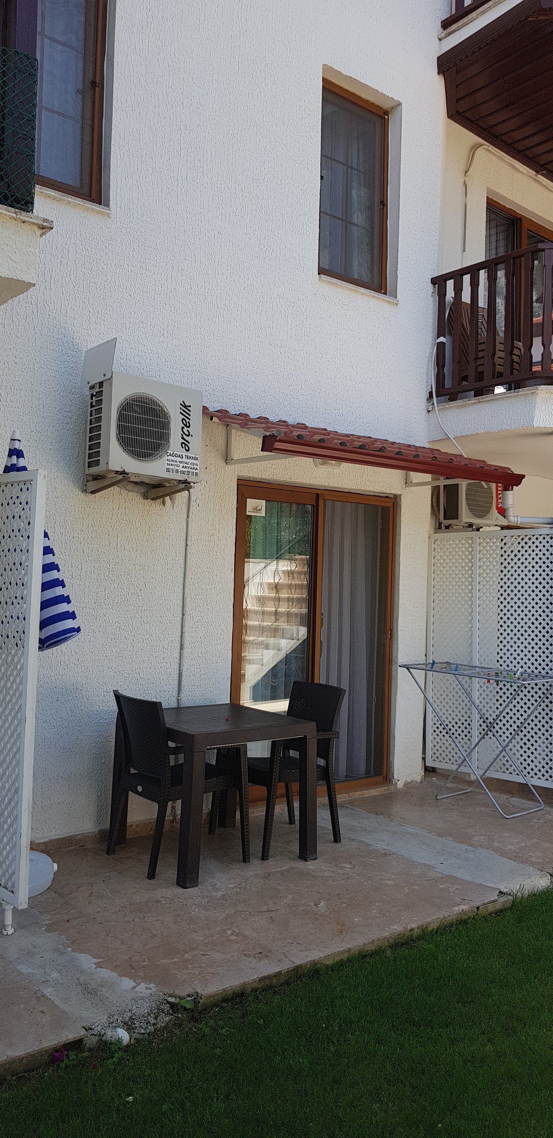 Un patio exterior con mesa y sillas, un equipo de aire acondicionado y una zona cubierta.