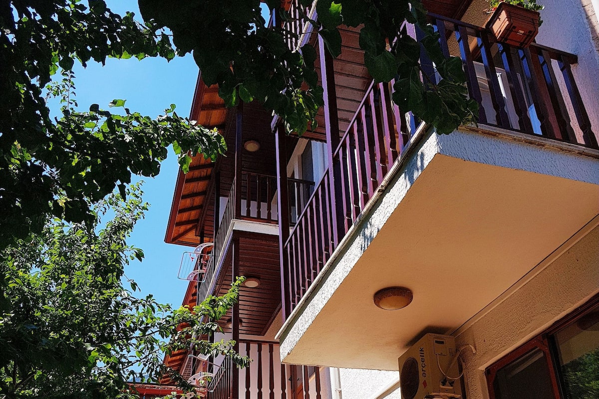 A residential building with a balcony, a small garden, and a door leading to the entrance.