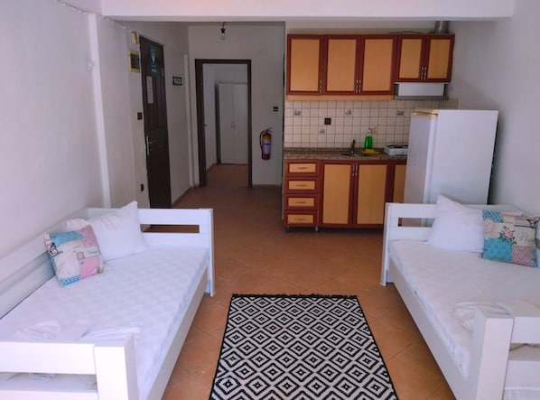 A compact room with two white beds, a kitchenette with wooden cabinets, and a patterned rug. - Santo Akyaka Home (Ula)